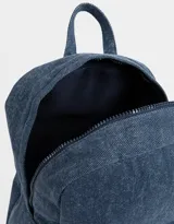 Mochila azul de denim con bolsillo frontal con cierre y tirador con charms decorativos. Tiene correas regulables, manija superior y cierre superior.