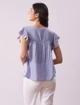 Blusa blanca de algodón con cuello a la base y escote en V con lazo de ajuste. Tiene mangas cortas con terminación amplia y bordados en delantera, mangas y espalda.