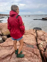 Piloto impermeable de color rojo con detalles de volados verdes en los hombros. Presenta capucha integrada, cintura ajustable con cordón, mangas con volumen y puños elastizados.