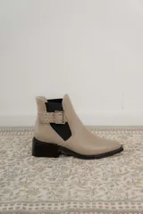 Botines Chelsea color beige con elásticos laterales negros, punta cuadrada, detalle de hebilla lateral y tacón bloque bajo.