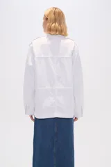 Chaqueta blanca de algodón con cuello camisero, cierre frontal con botones, bolsillos de parche y frunces en los hombros.