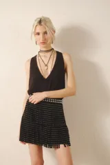 Falda corta negra de cuero con diseño de flecos y remaches metálicos plateados. La cintura es ancha y está adornada con tachas bombé.