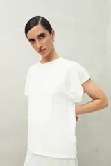 Top blanco de tejido texturizado con cuello redondo y mangas cortas tipo murciélago.