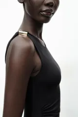 Vestido midi negro de punto, con cuello asimétrico, manga sisa, aplique metálico dorado en el hombro y drapeado lateral.