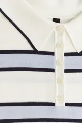 Remera polo de punto fino color blanco con rayas horizontales celestes y azul marino. Tiene cuello clásico, tapeta con botones y mangas cortas.