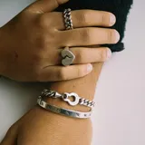 Pulsera rígida plateada con cierre de bisagra y grabados de líneas verticales.