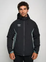 Campera corta de abrigo Umbro Crafted Pro, color negro con paneles laterales en gris. Presenta capucha con cordón ajustable, cierre frontal completo y logo de la marca bordado en el pecho.