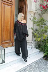 Vestido corto negro de tejido calado, con cuello desbocado y mangas largas. Incluye una tira tejida del mismo color con detalles de corazones dorados en los extremos.