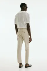 Pantalón tobillero color beige, de corte slim fit, con pliegues, cierre con botón, bolsillos laterales y bolsillos traseros ribeteados con botón.