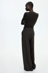 Pantalón ancho color marrón oscuro, de tiro alto con cierre, botón y corchetes ocultos, bolsillos al bies y bolsillos atrás decorativos. Piernas amplias con pliegue adelante y atrás.