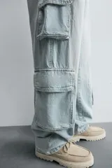 Pantalón de denim color beige, corte relaxed fit, con bolsillos laterales tipo cargo con solapa y cierre de botón. Cierre frontal con botón y cremallera.