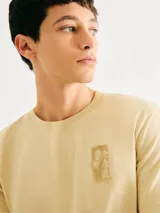 Camiseta blanca de algodón con cuello redondo y mangas cortas. Estampa rectangular con borde negro que contiene la frase "NATURAL ATMOSPHERE" en letras mayúsculas y una imagen de montañas y mar.