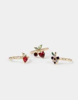 Set de tres anillos dorados con dijes de frutas con incrustaciones de strass: cerezas, frutilla y uvas.