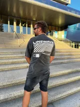 Remera negra con efecto gastado, corte amplio y estampado en la espalda con la palabra "Linewave" y un diseño de ondas blancas.