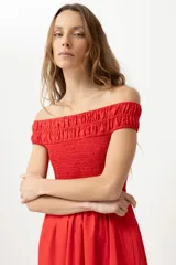 Vestido largo de color rojo con escote bardot y cuerpo elástico tipo nido de abeja. Presenta una falda de corte evasé con bolsillos laterales.