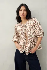 Blusa estampada color beige y blanco, con mangas abullonadas, escote redondo y lazos frontales.