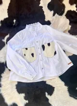 Camisa blanca de mangas largas con cuello mao con detalle de puntilla y dos bolsillos frontales con estampado animal print.