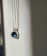 Collar con cadena plateada fina y dije circular con piedra azul engarzada en plata.