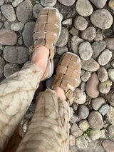 Sandalias de cuero marrón con diseño de tiras entretejidas y hebilla lateral.