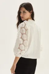 Blusa blanca de algodón con mangas abullonadas de broderie con diseño floreado. Presenta volados en el cuello y hombros, con un estilo romántico y femenino.