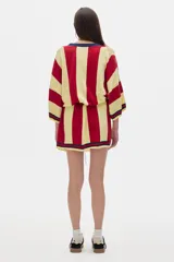 Bata tipo kimono a la rodilla, con rayas verticales rojas y amarillas y cuello en V azul marino. Tiene un logo bordado en el pecho y un lazo en la cintura.