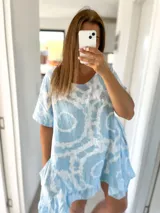 Vestido corto tipo túnica de lino rústico celeste con estampado batik blanco, corte holgado, mangas cortas y ruedo con volantes.