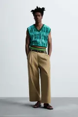 Pantalón color beige de corte ancho, con pliegues frontales dobles, bolsillos laterales y traseros de vivo. Largo cropped y cierre frontal con cremallera y botón.