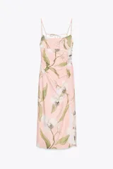 Vestido midi de tirantes finos, color rosa con estampado de flores blancas y hojas verdes. Tiene escote recto, detalle de frunces delanteros, forro interior, abertura frontal y cierre trasero con cremallera y botones.