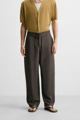 Pantalón marrón oscuro de corte amplio, con cintura ajustable con cordón, bolsillos plastrón delanteros y traseros, detalle de costuras frontales y cierre frontal con cremallera y gancho metálico oculto.