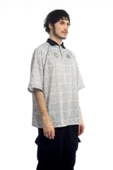 Remera deportiva blanca con cuello polo negro, cierre parcial con cremallera, mangas cortas y estampado de letras grises.