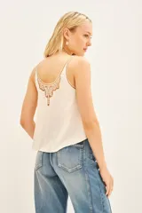 Top tipo musculosa color crema, confeccionado en modal satén, con escote en V decorado con un panel de calado y bordados a tono.