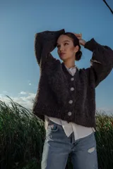 Cárdigan tejido de boucle color gris oscuro, con escote en V, mangas largas abullonadas y cierre frontal con botones grandes. Corte holgado.