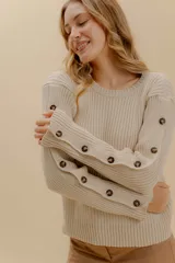 Sweater color beige de tejido de punto acanalado, con cuello redondo y mangas largas con detalle de botones en los puños.