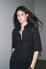 Camisa negra de manga corta confeccionada en hilatura con lyocell y ramio, con cuello solapa, bajo recto y cierre frontal con botones.
