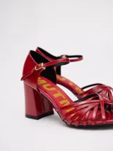 Sandalias negras de charol con tiras cruzadas en el empeine, pulsera con hebilla al tobillo y tacón cuadrado.