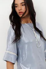 Blusa de lino color beige con brillo sutil, corte holgado, mangas cortas y cuello redondo.