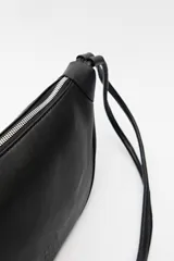 Bandolera color crema de símil cuero, con formato alargado y correa regulable con nudos.
