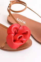 Sandalias bajas de cuero color suela, con tiras finas y aplique de flor roja en el empeine.
