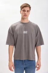Remera gris con estampa en la espalda que dice "Calm Vibes" con una flor en el medio. Corte amplio y recto, con proporciones cuadradas.