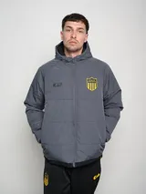 Campera de abrigo gris con capucha, cierre frontal y bolsillos laterales. Presenta costuras en contraste y escudo del Club Atlético Peñarol en el pecho.
