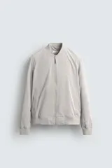 Cazadora bomber ligera gris confeccionada en tejido técnico. Cuello y puños en rib elástico, manga larga, bolsillos de vivo en cadera y bolsillo interior. Cierre frontal con cremallera.