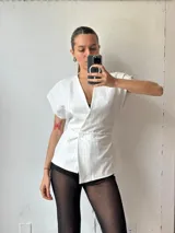 Chaleco blanco con finas rayas verticales celestes, escote en V, corte ajustado y cierre frontal con un botón.