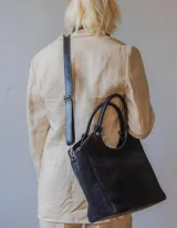 Cartera negra de gamuza con forro interior y correa larga desmontable.
