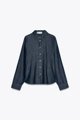 Camisa de denim azul oscuro, corte amplio, cuello solapa, manga larga y cierre frontal con botones a presión.