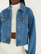 Chaqueta cropped de denim azul con mangas largas y cierre de botones. Tiene bolsillos con solapa y corte recto.