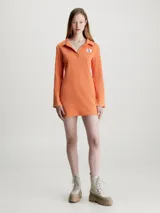 Vestido corto naranja de punto de algodón elástico con textura de canalé. Tiene cuello polo en V, mangas largas acampanadas e insignia con el monograma de Calvin Klein en el pecho.