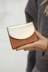 Monedero pequeño de cuero en tonos tostados y plateados, con diseño compacto y cierre de solapa.