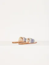 Sandalia chata confeccionada en denim, con flecos en la capellada y aplique metálico.