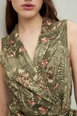 Vestido midi sin mangas con estampado floral y de hojas en tonos verde y marrón. Diseño cruzado tipo wrap con cuello sastrero y lazo ajustable en la cintura.