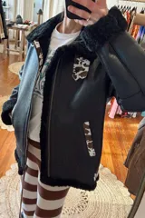 Campera bomber de cuero negro con interior de piel sintética color crema. Presenta cierre frontal, cuello y puños de piel sintética y apliques de cuero con estampado animal print.